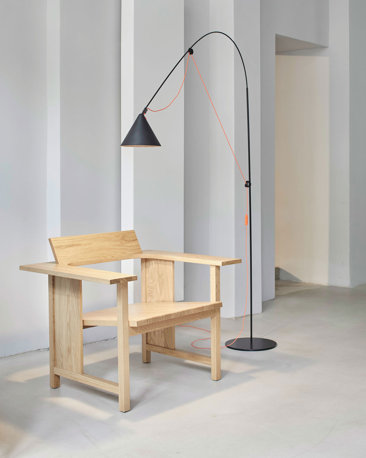 Midgard AYNO L floor lamp in black with neon orange textile cable in an interior with modern arm chair