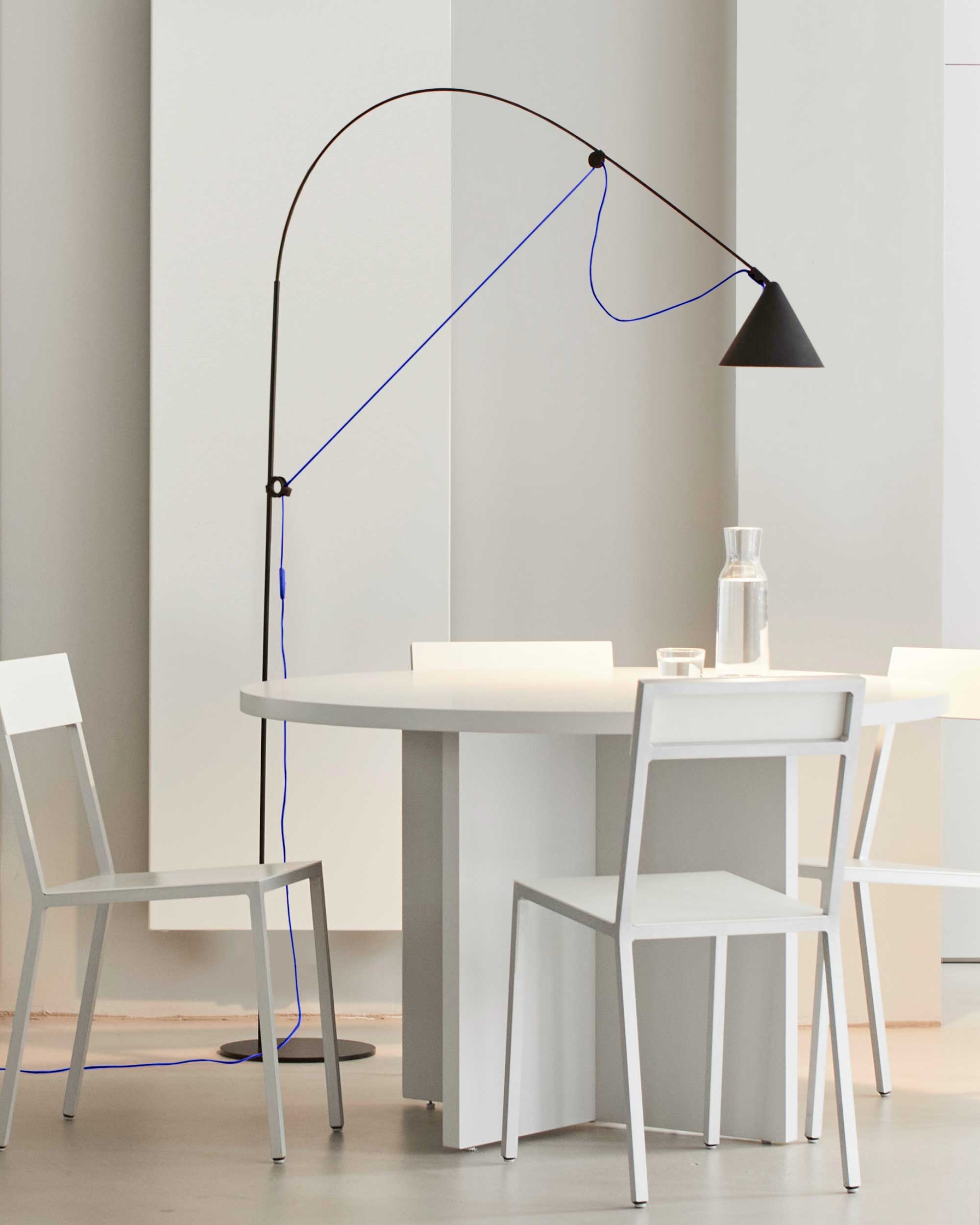 Midgard AYNO L adjustable floor lamp in black with ultramarine blue cable beside a dining table