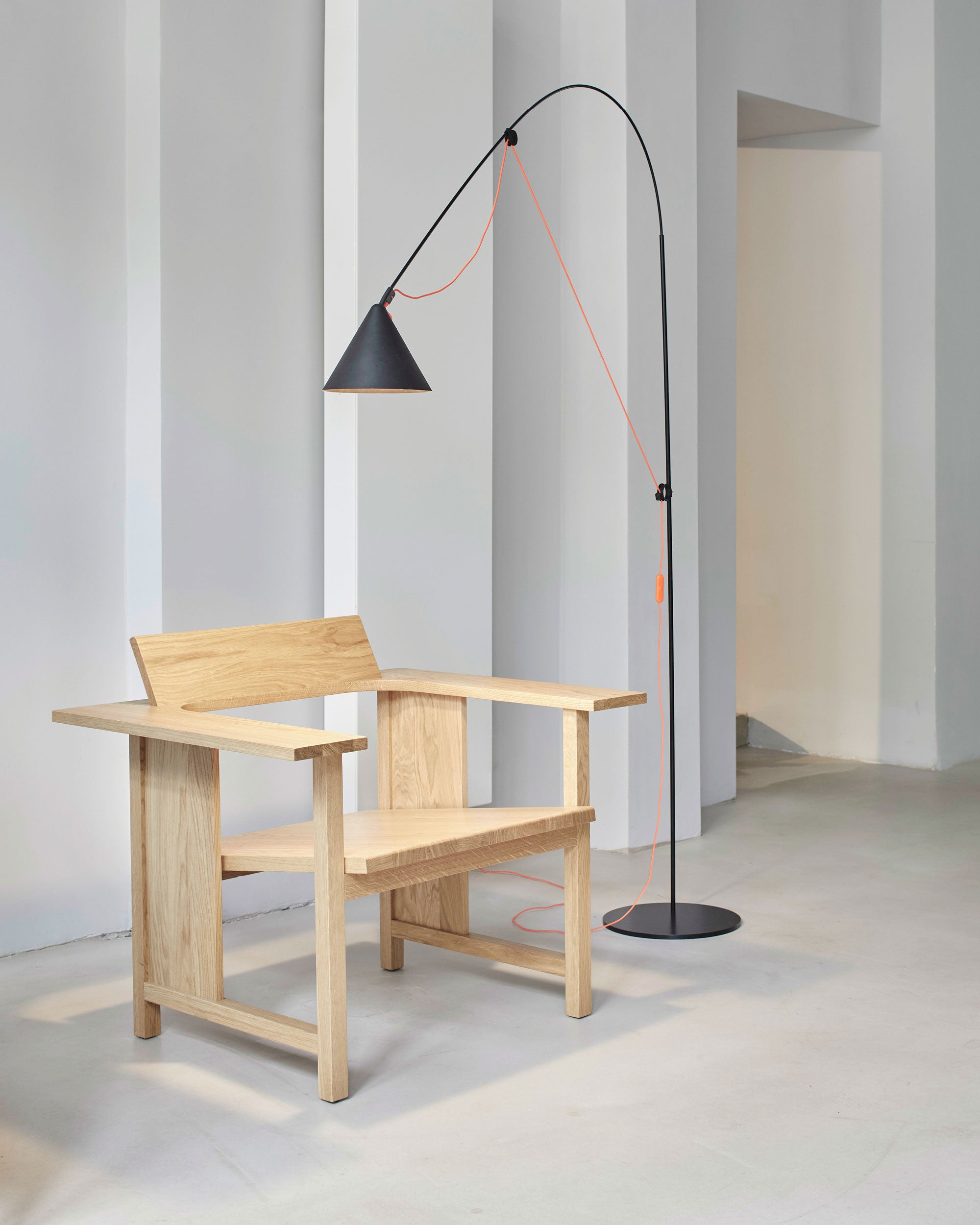 Midgard AYNO L floor lamp in black with neon orange textile cable in an interior with modern arm chair