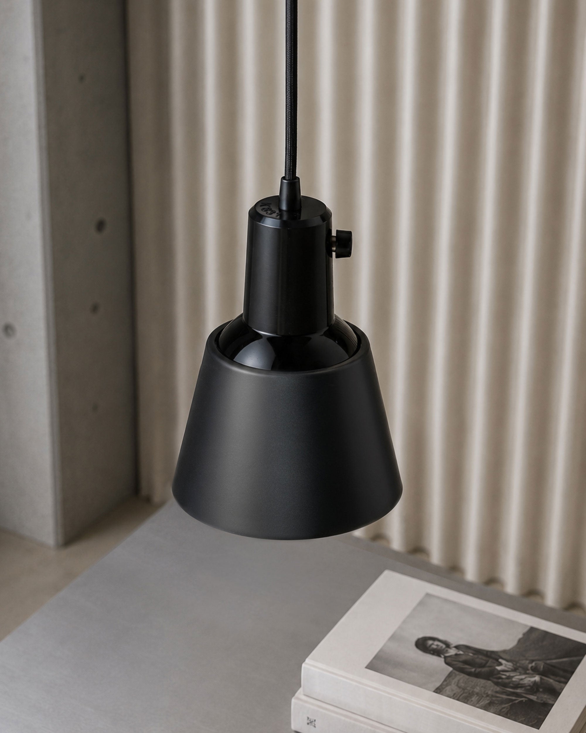 Midgard K831 pendant lamp in powder-coated black suspended above a side table in a contemporary interior.