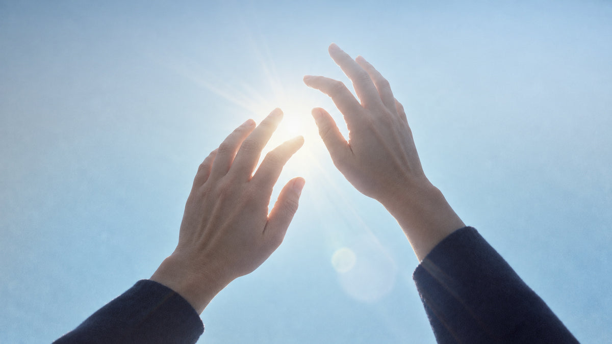 Hands reaching towards sunlight under a blue sky